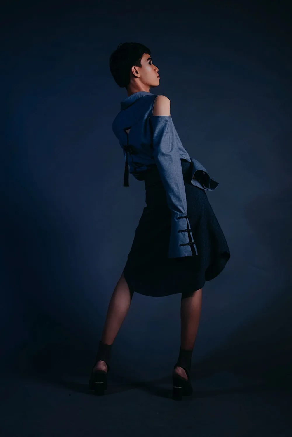 Model in blaugrauem Mantel vor dunkler Studiowand