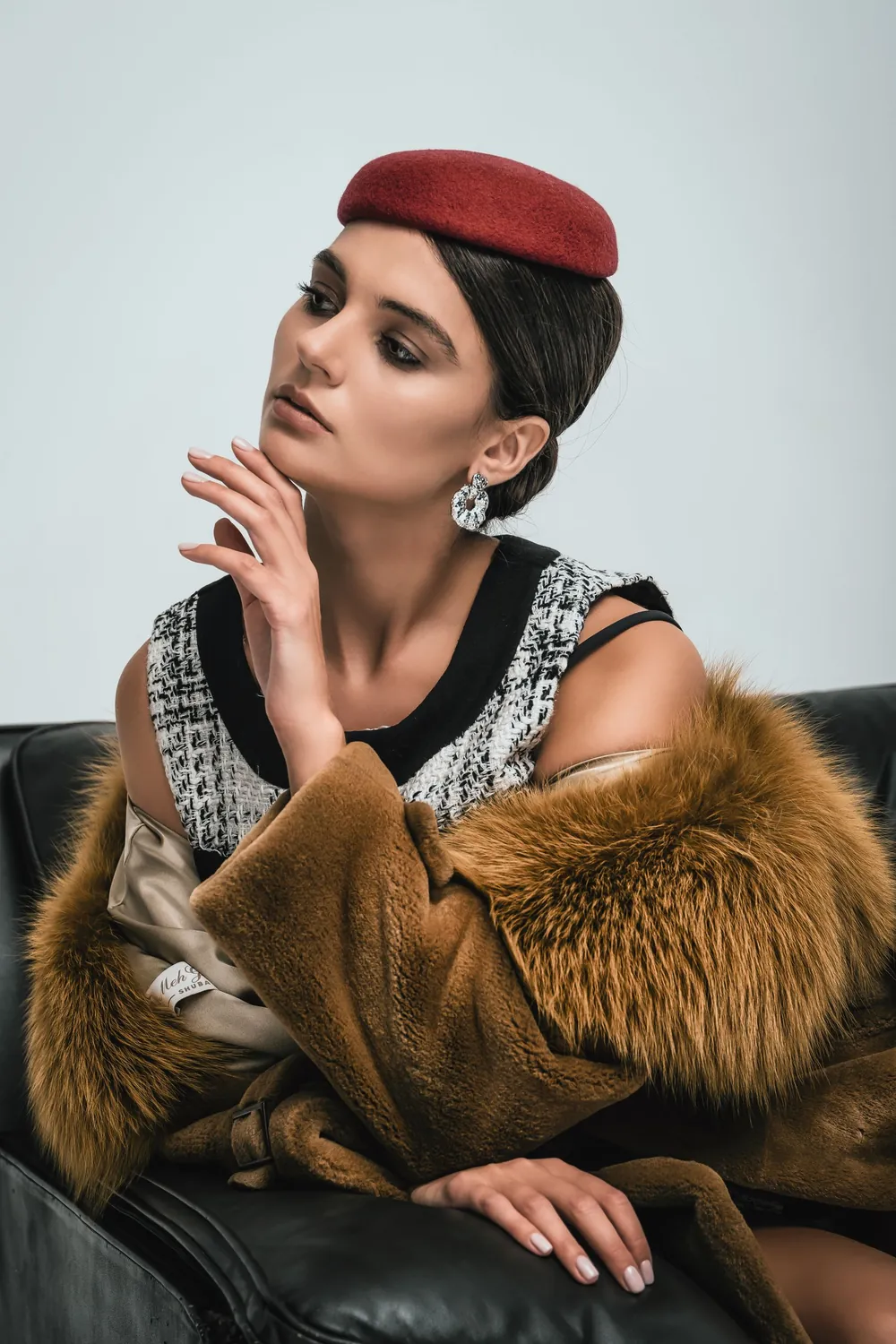 Portrait einer Frau mit rotem Barett und Pelzmantel auf einem Ledersofa
