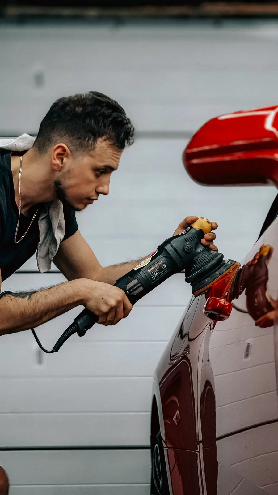 Deniz poliert konzentriert die Flanke eines roten Autos mit einer Poliermaschine