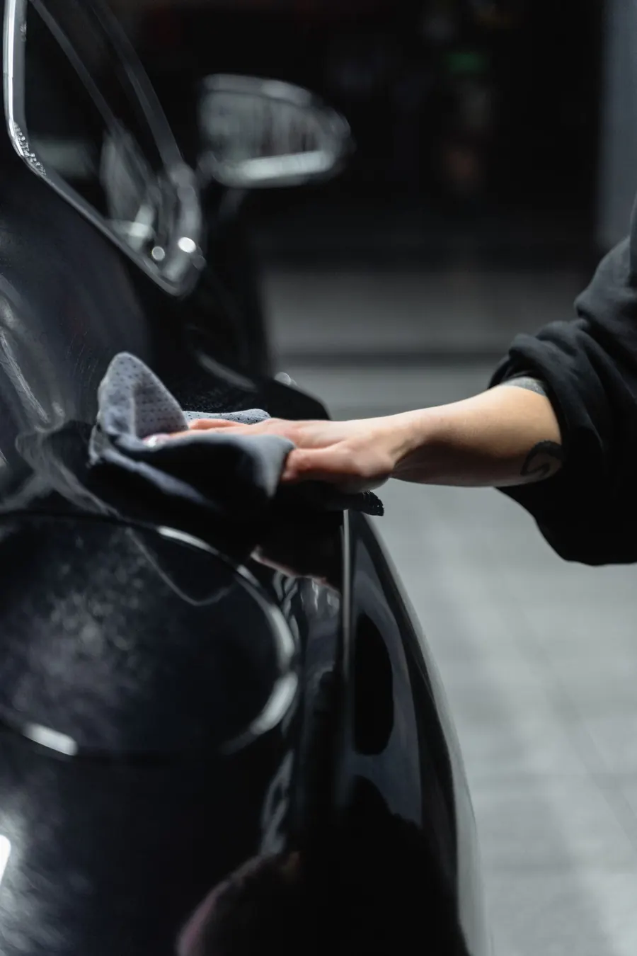 Hand poliert die Flanke eines schwarzen Autos mit einem grauen Mikrofasertuch